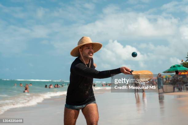 uomo che gioca a paddleball sulla spiaggia - cappello per il sole foto e immagini stock