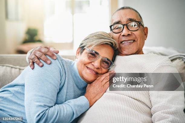 aufnahme eines älteren paares, das sich zu hause auf der couch entspannt - senior woman smiling at camera portrait stock-fotos und bilder