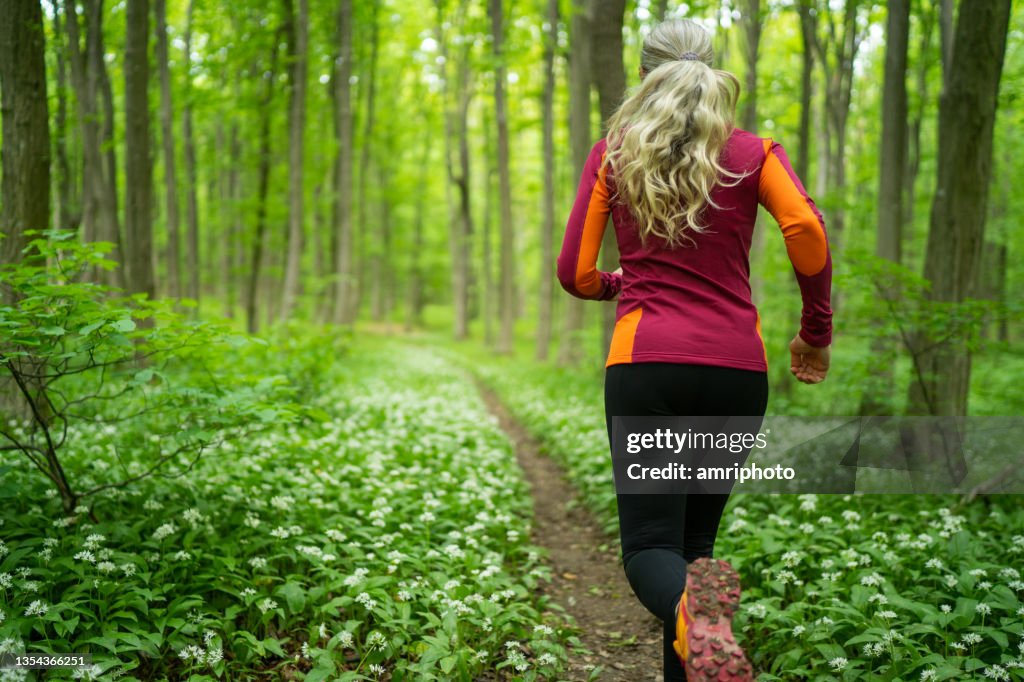 Rückansicht Frau joggt im Frühling durch Wald