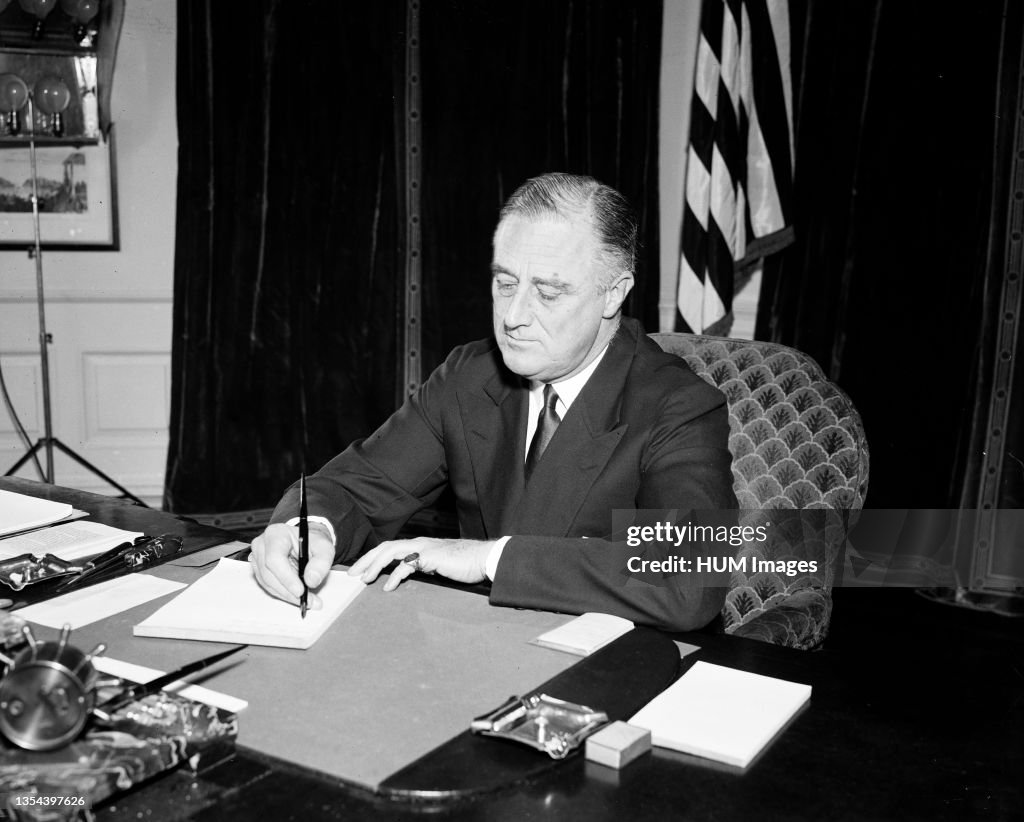 President Franklin Roosevelt sitting at a desk and signing a piece of paper ca. 1934