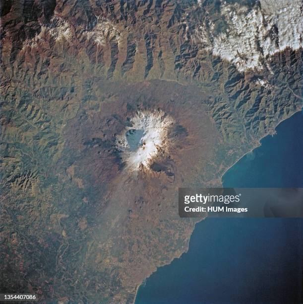 Thin plume of steam blows southward from the summit of Mt. Etna, the active volcano on the island of Sicily. The summit is capped with snow but the...