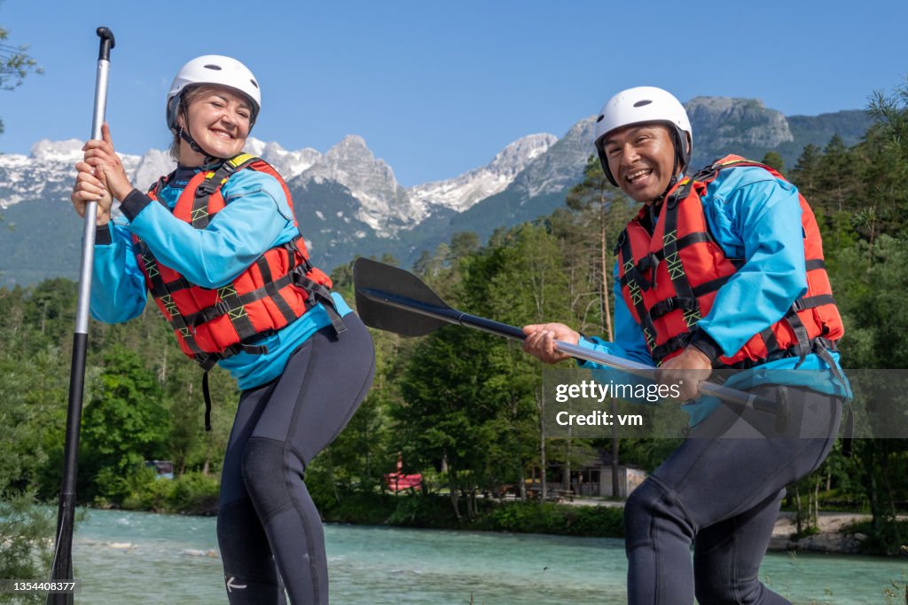 Alegre pareja sonriente posando en la orilla del río, azotando el trasero de la mujer con remo