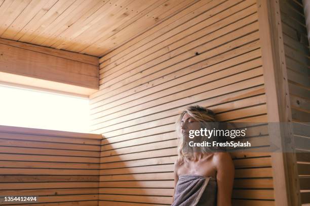 スパデー:グレーのタオルに包まれたサウナに座っている美しい若いブロンドの女性 - sauna ストックフォトと画像