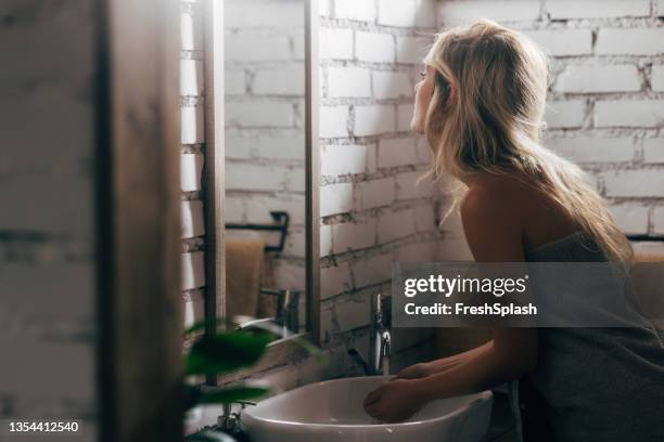 schöne blonde frau, die sich die hände im waschbecken wäscht - wrapped in a towel stock-fotos und bilder