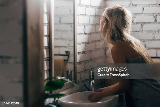 beautiful blonde woman washing her hands in the bathroom sink - woman in bathroom stock pictures, royalty-free photos & images