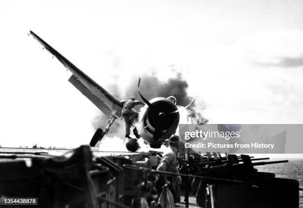 Crash landing of F6F on the flight deck of the USS Enterprise while enroute to attack Makin Island. Lt. Walter Chewning, catapult officer, clambering...