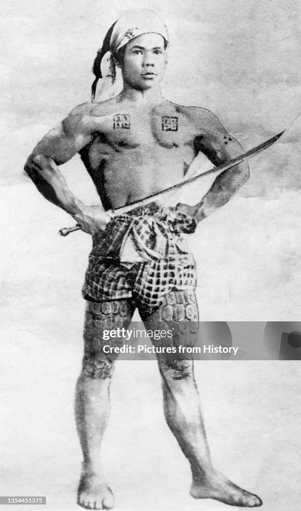 A tattooed young man poses as a warrior and flexes his muscles for the camera in Mong Un, Shan State.