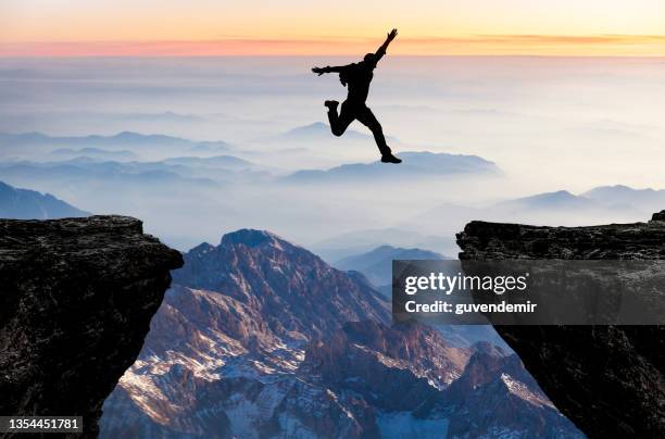 silhouette of man jumping from one cliff to another cliff with excitement - penhasco caraterísticas do território imagens e fotografias de stock