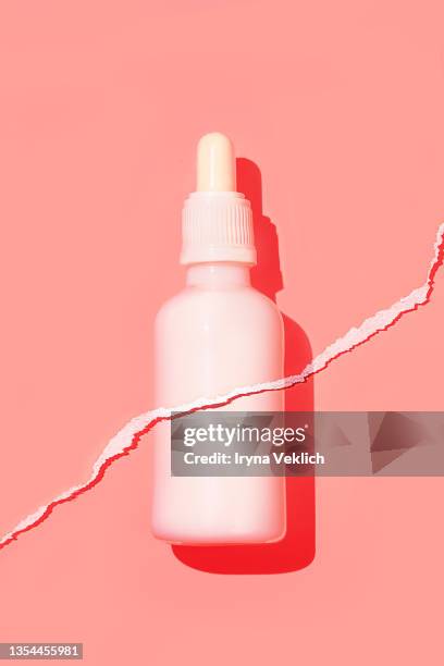 white bottle of organic moisturizing facial serum or essential oil on pastel pink coral color background with torn paper effect. routine step for healthy skin care. - retinol stock pictures, royalty-free photos & images