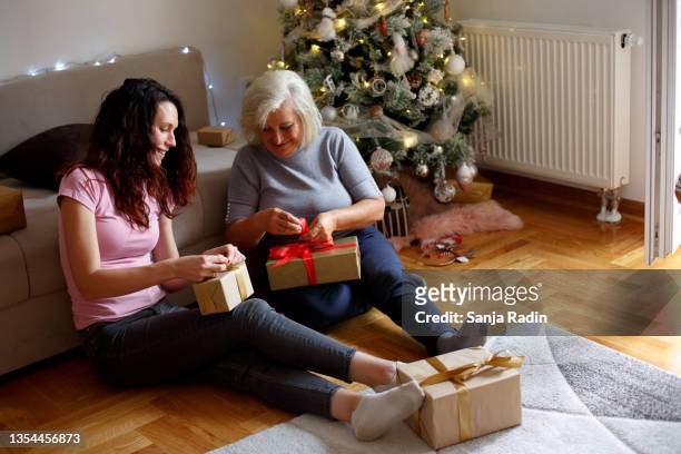 a young woman and her mother are on the floor, in the living room, opening presents. new year's day. - 30 year old men stockfoto's en -beelden