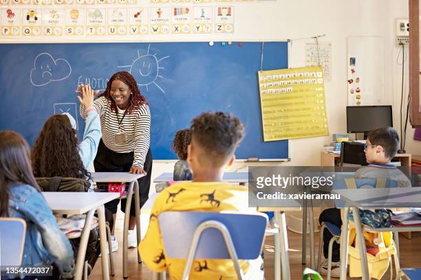 teacher and schoolgirl exchanging high-five in classroom - students demonstrate in favour of free education stockfoto's en -beelden