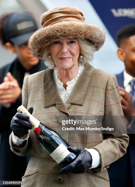 Camilla, Duchess of Cornwall holds a bottle of champagne as she presents the prizes to the winners of the 'Ebony Horse Club Novices' Limited Handicap...