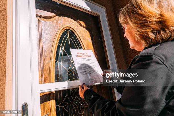 middle-age woman holding a foreclosure notice at the front door of a home in a residential suburban neighborhood - foreclosure 個照片及圖片檔