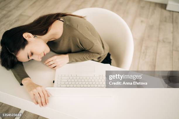 beautiful young woman with long brown hair closed eyes, lay down on the table and fell asleep. she was working at home office using laptop and was very tired. concept of remote work - woman sleeping table stock pictures, royalty-free photos & images