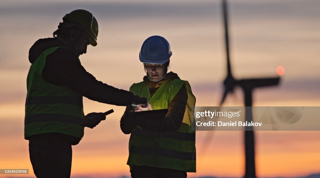Wind energy engineers working in wind farm at dusk. Renewable Energy Systems. Carbon neutrality and sustainable energy.