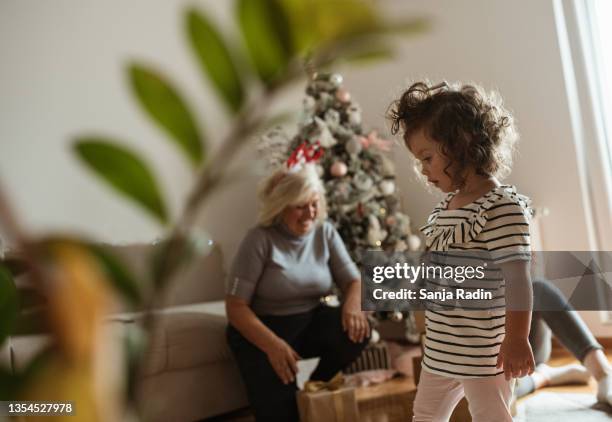 a cute little girl with curly hair is standing in the middle of the living room, awaiting to get a present from her granny. christmas decoration. - blurry living room stockfoto's en -beelden