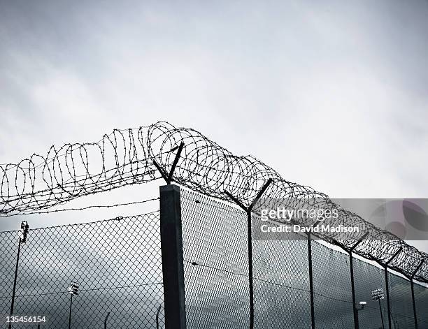 chain link fence with barbed wire and razor wire. - fil barbelé photos et images de collection