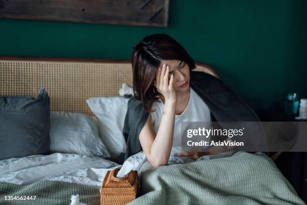 young asian woman feeling sick with hands on stomach, lying on the bed and taking a rest at home - anaemia stock pictures, royalty-free photos & images