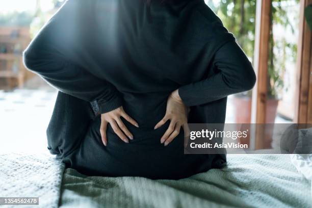 vista trasera de una mujer que sufre de dolor de espalda, masajeando los músculos doloridos mientras está sentada en la cama - sciatic nerve fotografías e imágenes de stock