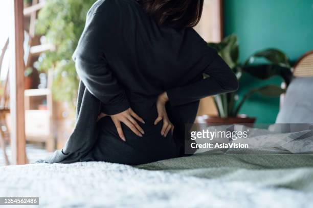 rear view of woman suffering from backache, massaging aching muscles while sitting on bed - back pain bed stock pictures, royalty-free photos & images
