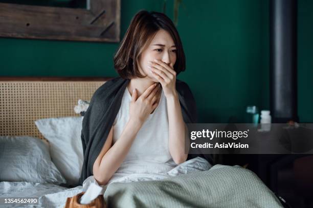 young asian woman feeling sick, suffering from sore throat, feeling sore and hurt, staying at home and resting on bed - woman cough stock pictures, royalty-free photos & images