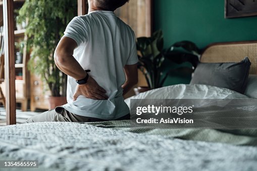 Vista posteriore dell'uomo asiatico anziano che soffre di mal di schiena, massaggiando i muscoli doloranti mentre è seduto sul letto. Concetto di anziani e problemi di salute Vista posteriore dell'uomo asiatico anziano che soffre di mal di schiena, massaggiando i muscoli doloranti mentre è seduto sul letto. Concetto di anziani e problemi di salute