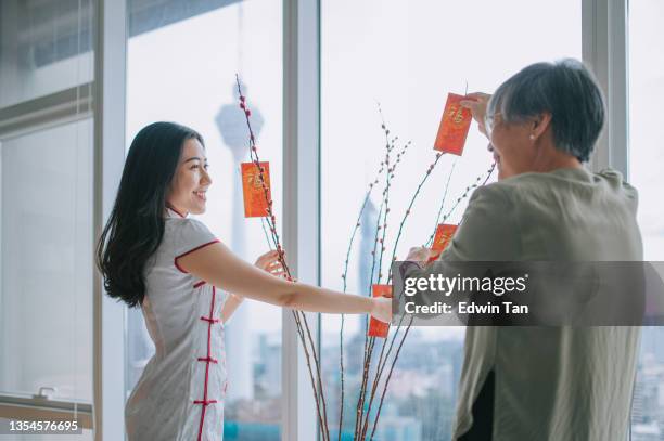 chinese new year senior woman and her daughter decorating house living room with pussy willow and red packet ang pao decoration preparing for family reunion - chinese prepare for lunar new year stock pictures, royalty-free photos & images