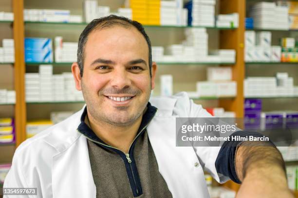 portrait of a cheerful handsome pharmacist leaning on counter at drugstore - mid adult men stock pictures, royalty-free photos & images
