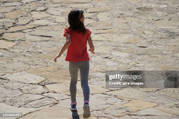 little girl with ink shirt walking on cobblestone ground on a sunny day - girls in leggings stock-fotos und bilder