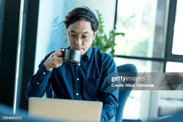 japanese entrepreneur drinking a coffee during a video conference with a partner on a laptop in a co-working space. iot solution and cloud computing for remote office. - managing director office stock pictures, royalty-free photos & images