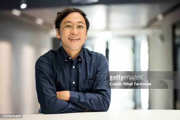 portrait of a japanese entrepreneur standing with his arms crossed in a modern office. small business entrepreneurship. - business man portrait smiling stock-fotos und bilder