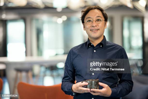 portrait of a confident japanese businessman in a modern office while holding a coffee mug during a break. - asian ceo stock-fotos und bilder