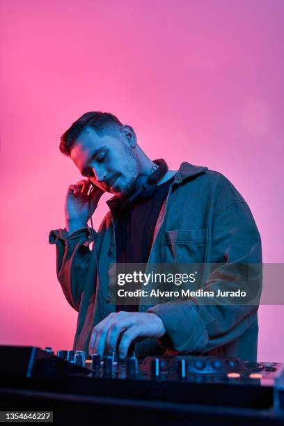 young male dj playing music in a session with red and blue lighting backgrounds. - headphones turntable stock-fotos und bilder
