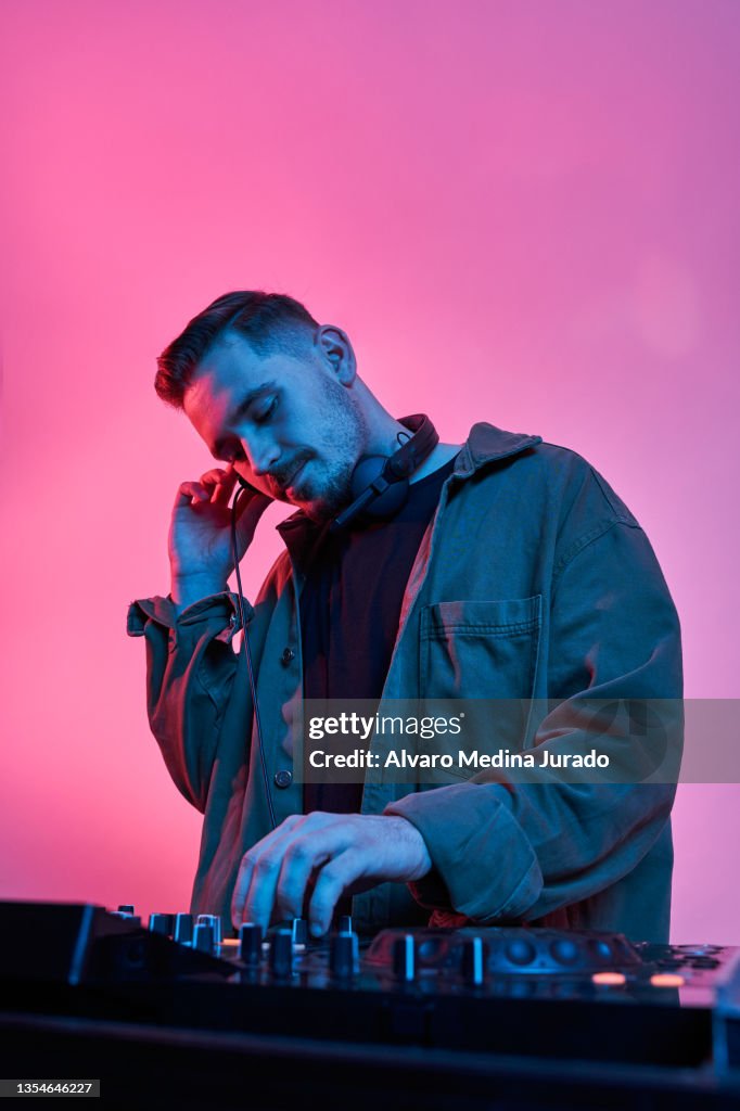 Young male DJ playing music in a session with red and blue lighting backgrounds.