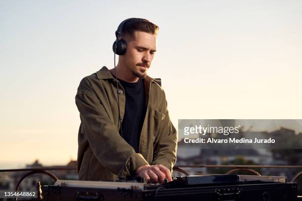 young male dj playing music in a session with a mixer at a sunset party on a rooftop. - dj de club fotografías e imágenes de stock