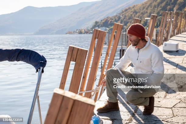 young man docking boat on lake in autumn - moored stock pictures, royalty-free photos & images