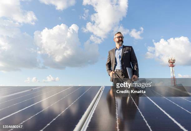 portrait of businessman holding laptop with standing on rooftop which install photovoltaic panel system. - solar system stock-fotos und bilder
