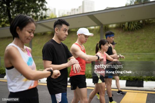 los atletas chinos asiáticos que hacen cola para prepararse para comenzar a cronometrar usando el reloj inteligente trazador de fitness antes de correr. - lining up sports activity fotografías e imágenes de stock