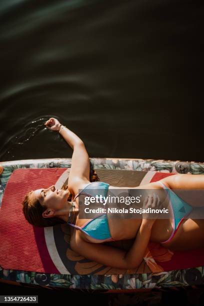 a woman is sunbathing on a paddle board - surf tube stock pictures, royalty-free photos & images