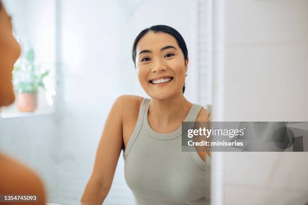 morning routine: portrait of a beautiful asian woman looking at herself in the mirror holding a beauty care product - mongolian women stock pictures, royalty-free photos & images