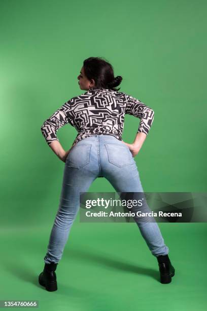 beautiful woman of size l with a little overweight poses on green background with casual clothes and has fun, rear end pose - woman bum stock-fotos und bilder