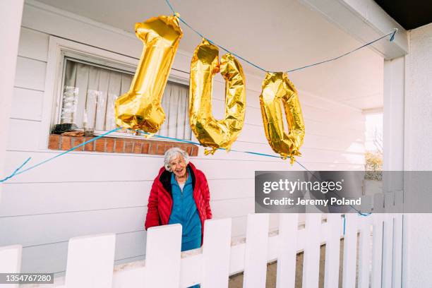 plan grand angle d’une femme âgée caucasienne âgée et joyeuse célébrant son 100e anniversaire avec des ballons dorés - centième anniversaire photos et images de collection