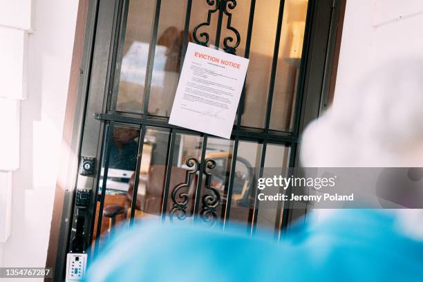 donna anziana di 100 anni con i capelli bianchi in piedi e guardando un avviso di sfratto sulla porta d'ingresso di una casa - information sign foto e immagini stock
