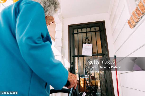 mulher idosa de 100 anos em pé e olhando para um aviso de despejo na porta da frente de uma casa - despejo - fotografias e filmes do acervo