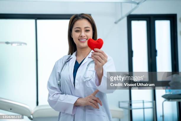 young woman doctor holding a red heart at hospital office. - asian violence stock pictures, royalty-free photos & images