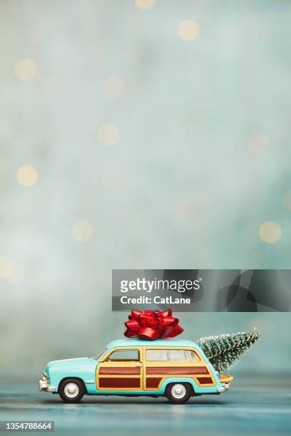 christmas background with vintage station wagon car with christmas tree in trunk and bow on rooftop - blue winter tree stockfoto's en -beelden