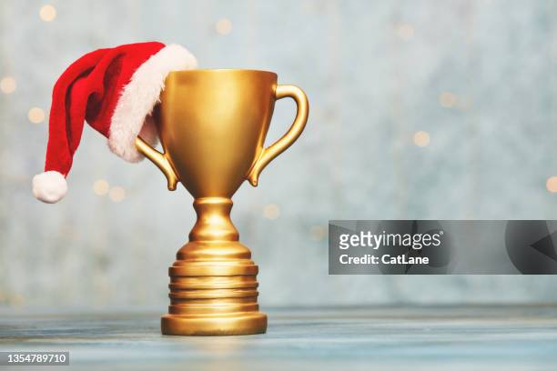 goldene trophäe mit weihnachtsmütze vor dem hintergrund mit weihnachtsbeleuchtung. weihnachtspreis oder gewinnerkonzept - victory lane stock-fotos und bilder
