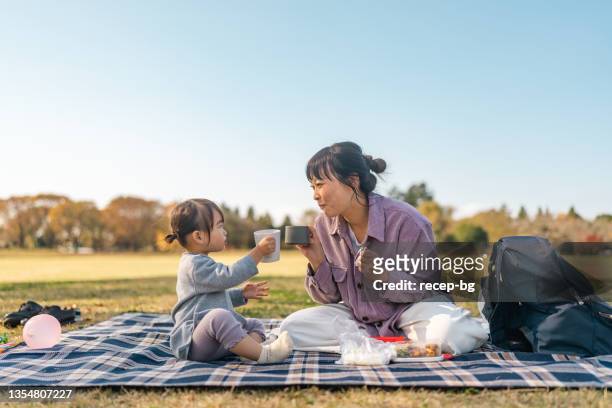 mother and daughter enjoying having picnic together in public park on warm sunny day - 野餐 個照片及圖片檔