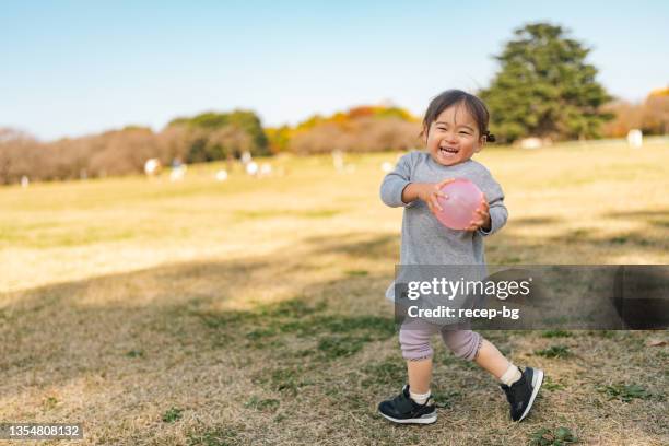 cute small girl running and playing in public park on sunny day - ballkid stock pictures, royalty-free photos & images