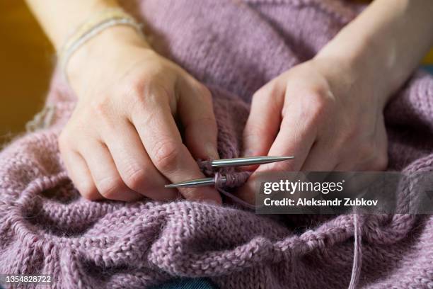 the girl is holding a knitting project and metal knitting needles in close-up. a woman knits a blue wool sweater or scarf, sitting on the couch at home. the concept of hobbies, creativity, needlework and manual work. creating clothes with your own hands. - mani fili foto e immagini stock